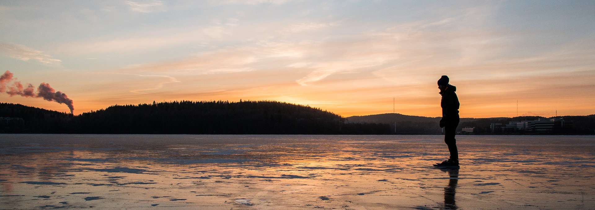 Silluetten av en skridskoåkare på en isbelagd sjö. Bilden är tagen i solnedgång.