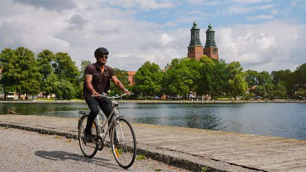 Man på cykel intill Eskilstunaån med Klosters kyrka i bakgrunden