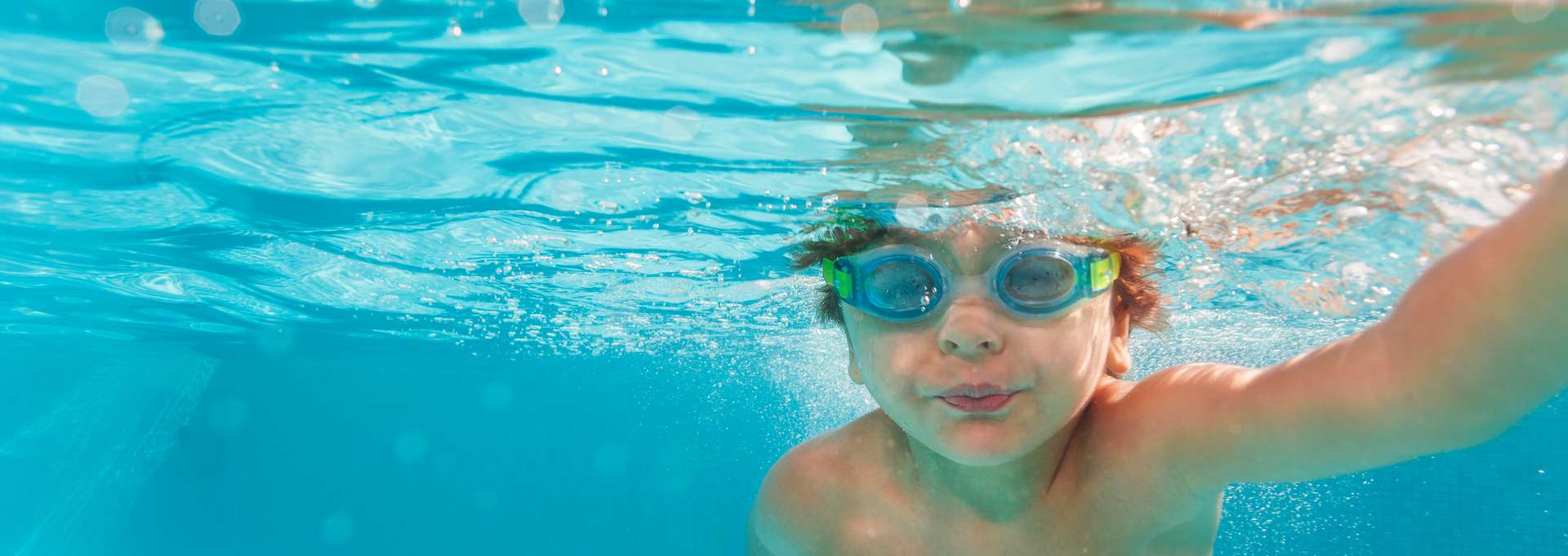 Small boy swimming wearing goggles under the crystal-clear water of swimming pool - underwater shoot
