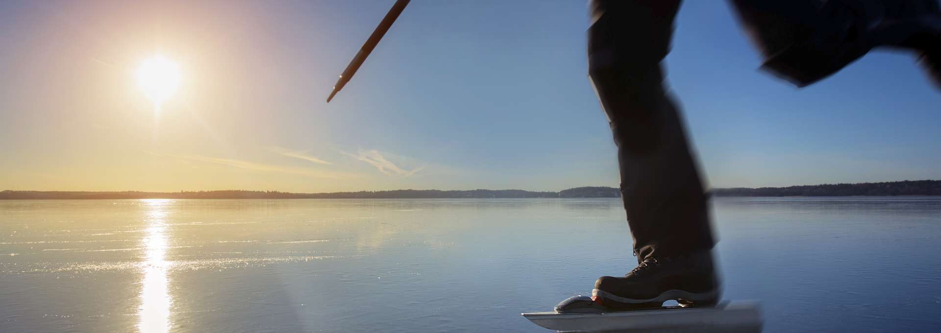 Person på långfärdskidor på en sjö. Solen skiner.