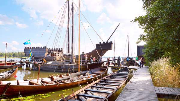 Tre vikingabåtar ligger vid en bryggan en solig sommardag. 