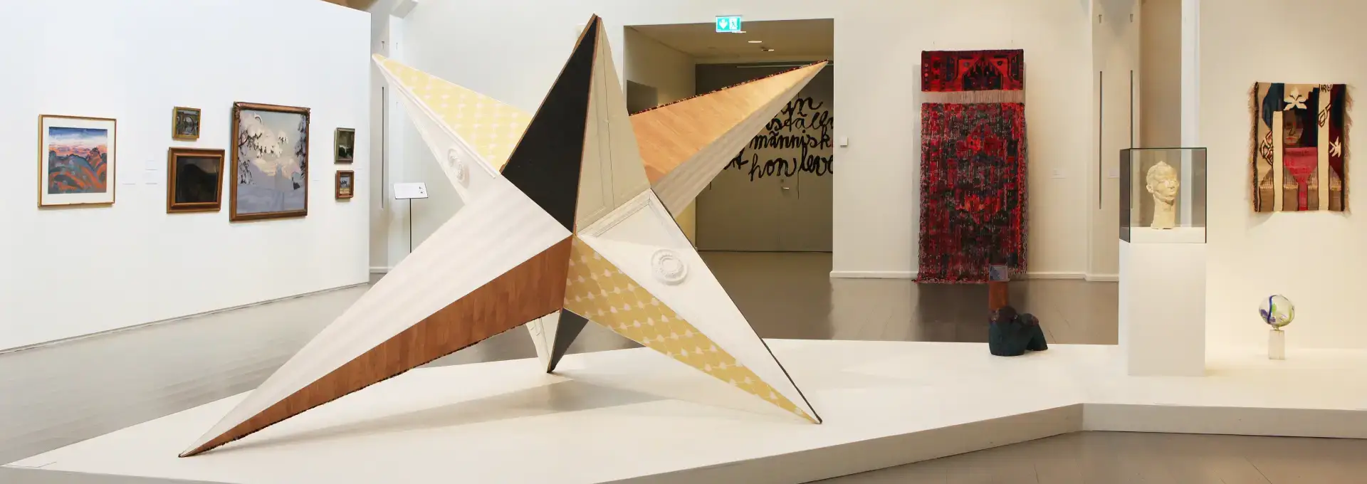 Flera konstverk i en utställningshall med en tredimensionell stor stjärna i mitten.