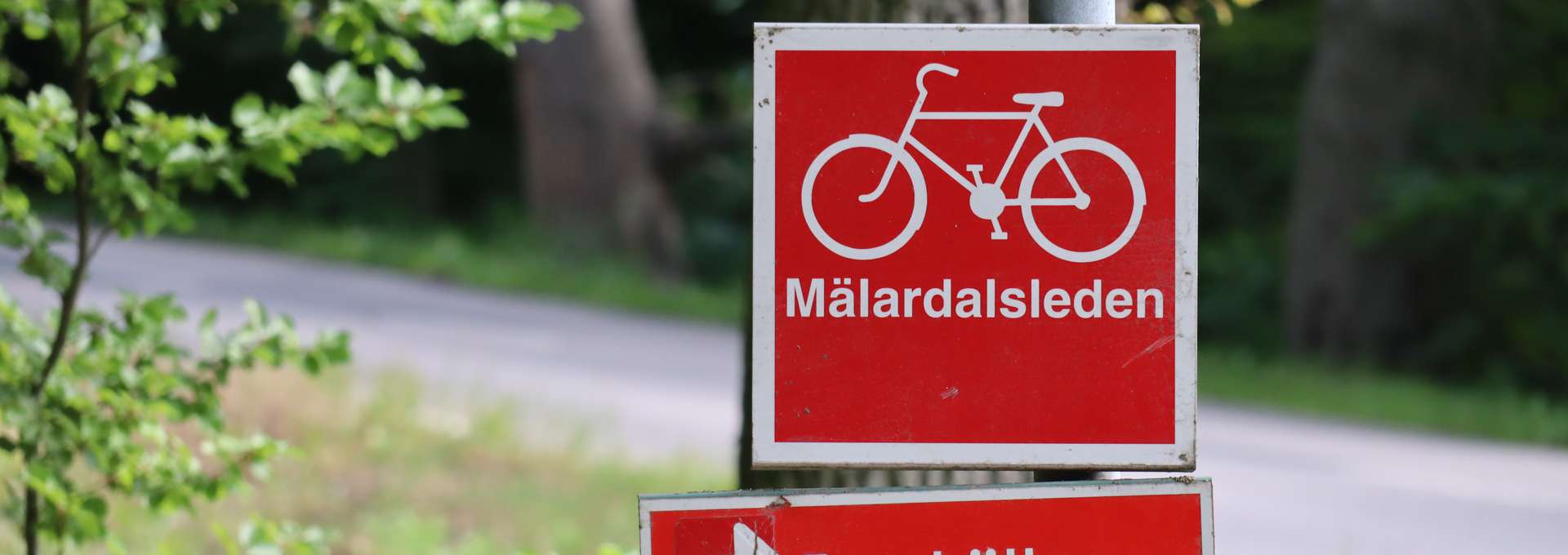 A red street sign with a white bike on it and the text Mälardalsleden 